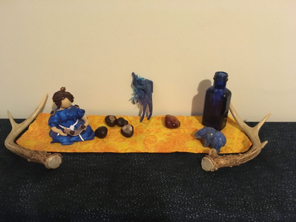 A photograph of various decorative altar items on a yellow cloth sitting on a dark blue cloth, with antlers curving around both sides. Described in surrounding text.