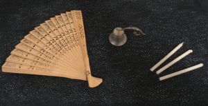 Photograph of wooden fan, candle snuffer, and three small candles for lighting other candles.